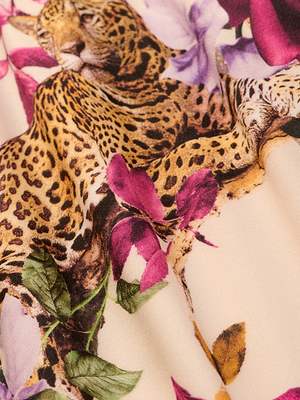 A close-up of the Violet String Bikini Bottoms fabric, showcasing a rose leopard print with a resting leopard among purple and pink flowers, green leaves, and subtle chain accents on a light beige background.