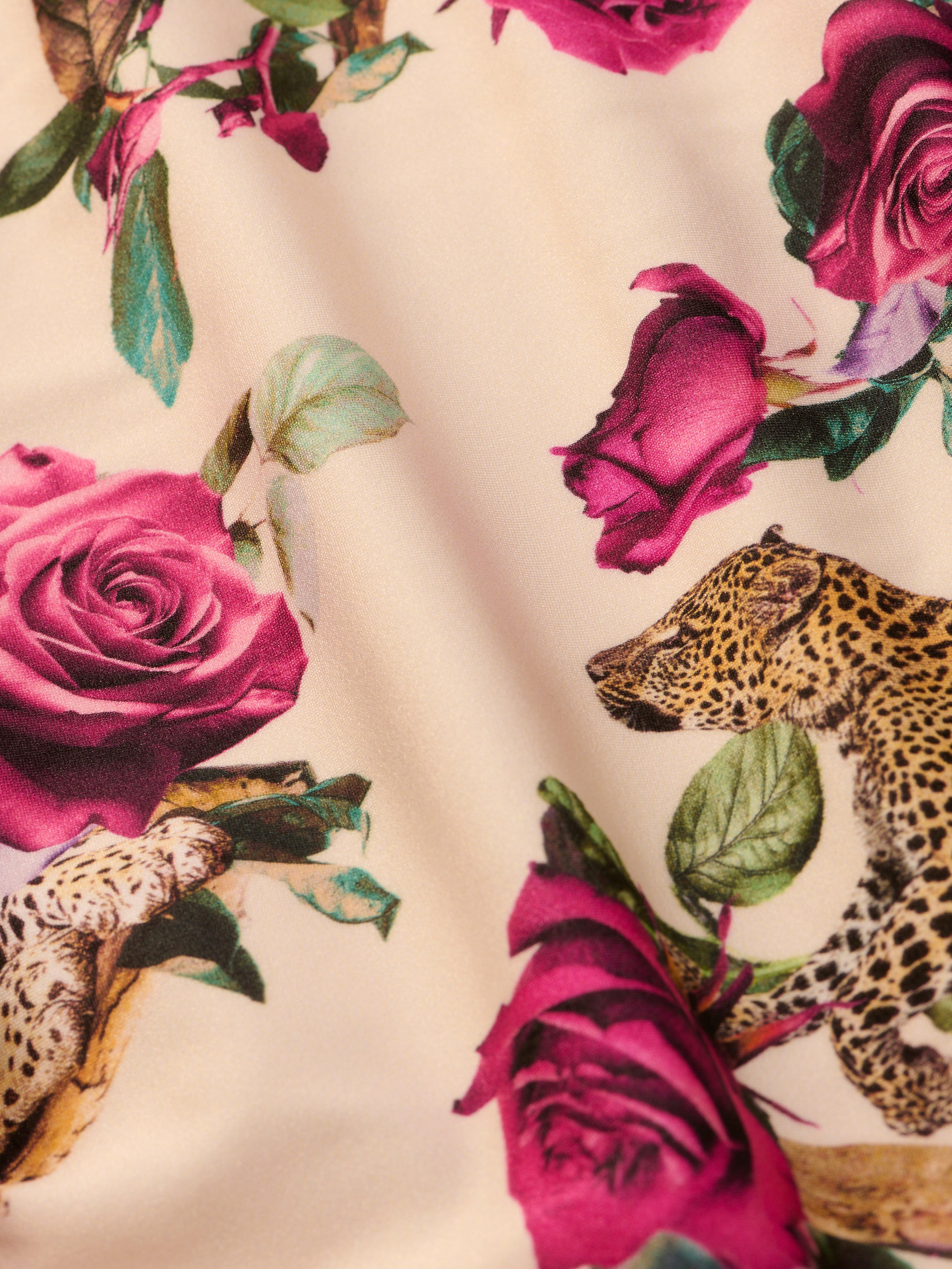 The Vanessa High-Waisted Bikini Bottom showcases a playful blend of pink roses and green leaves intertwined with leopard heads and legs, all set against a light beige background. This unique bikini bottom features an artistic rose leopard print that fuses floral and animal motifs for a colorful, stylish look.
