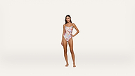 A woman stands on a plain white background wearing a colorful, patterned one-piece swimsuit. She has one hand on her hip and is facing the camera, smiling slightly.