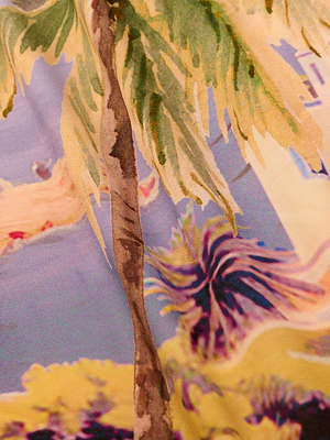 A close-up of the Maribel Cover-Up Pareo, showing its vibrant tropical design with a painted palm tree, yellow-green leaves, and abstract shapes in purple, blue, and yellow—perfect for sunny days.