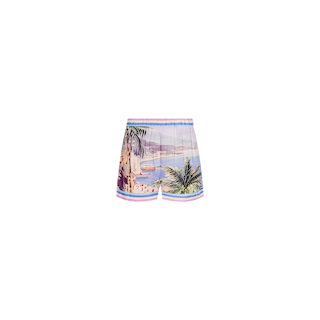 The Enyo Cover-Up Short features a vibrant coastal postcard print with palm trees, water, mountains, and buildings. These colorful vacation shorts include an elastic waistband and pink trim at the waist and legs, shown against a plain white background.