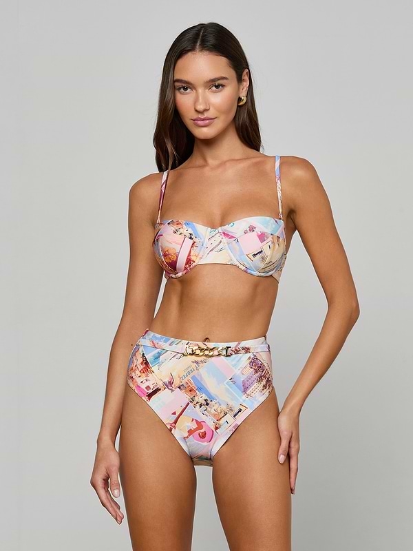 A woman stands against a plain white background, facing forward with a relaxed expression, wearing the Alexandria Bikini Top—a colorful, high-waisted bikini set featuring a postcard print and offering UPF 50 protection through its balconette-style design.
