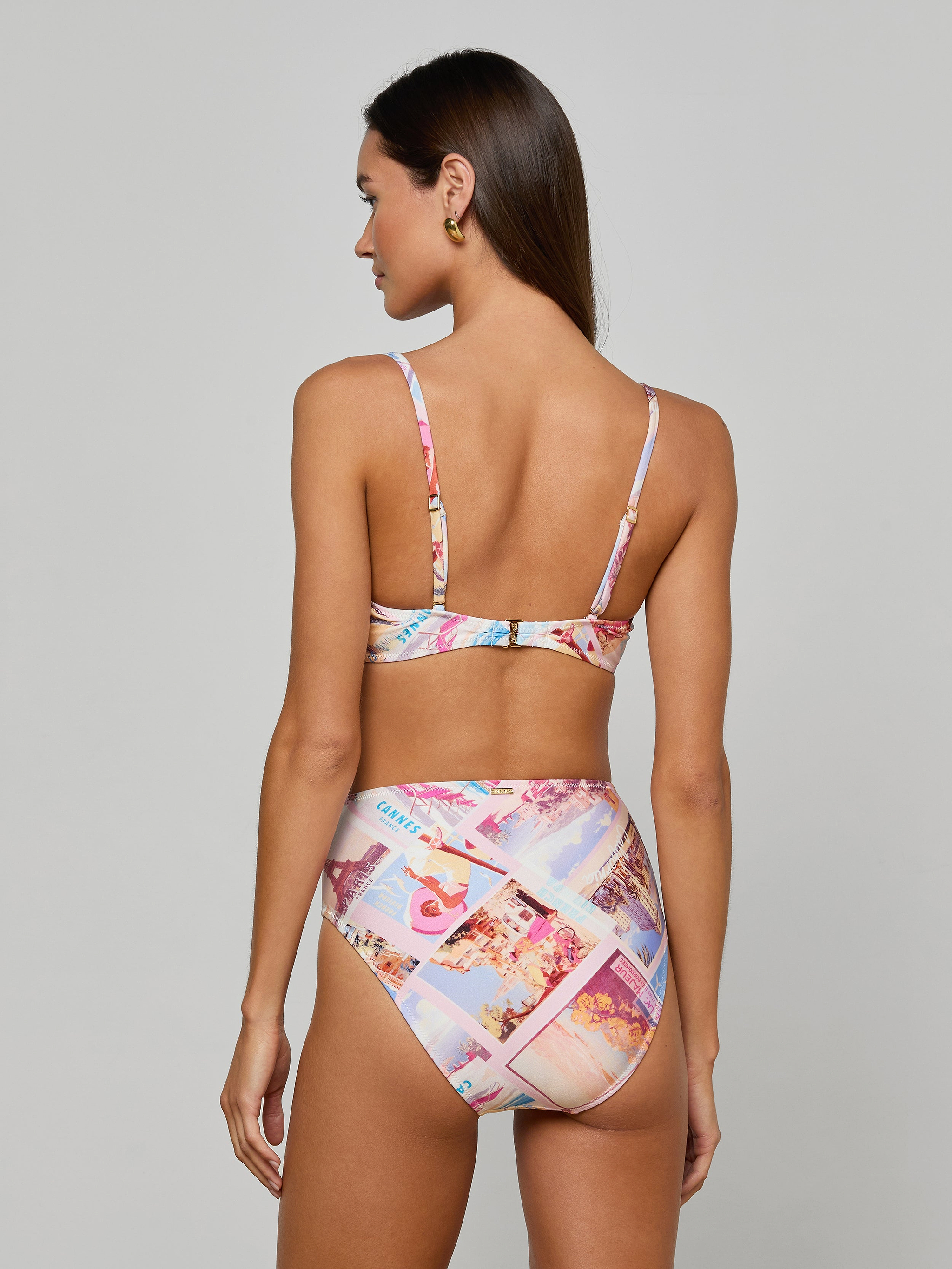 Woman with long brown hair, seen from the back and standing against a plain light background, wearing the Alexandria Bikini Top—a colorful, balconette swim top in a high-waisted bikini set featuring postcard print.