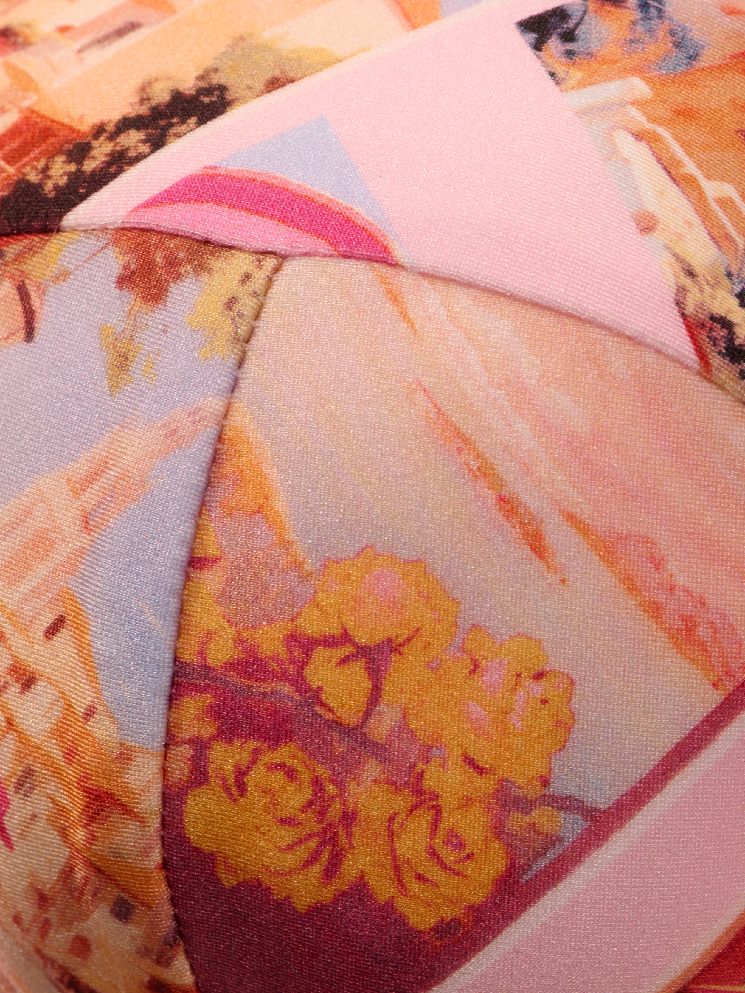 Close-up of the Alexandria Bikini Top, featuring colorful, patterned fabric with abstract shapes and floral prints in shades of pink, yellow, and orange—reminiscent of a vibrant postcard print—and detailed stitched seams.