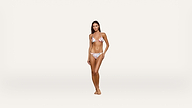 A woman stands confidently in a floral bikini against a plain white background, looking at the camera with a relaxed pose and natural expression.
