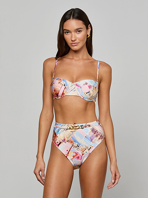 A woman with long brown hair models the Vanessa High-Waisted Bikini Bottom and a balconette top in a postcard print, standing against a plain gray background.