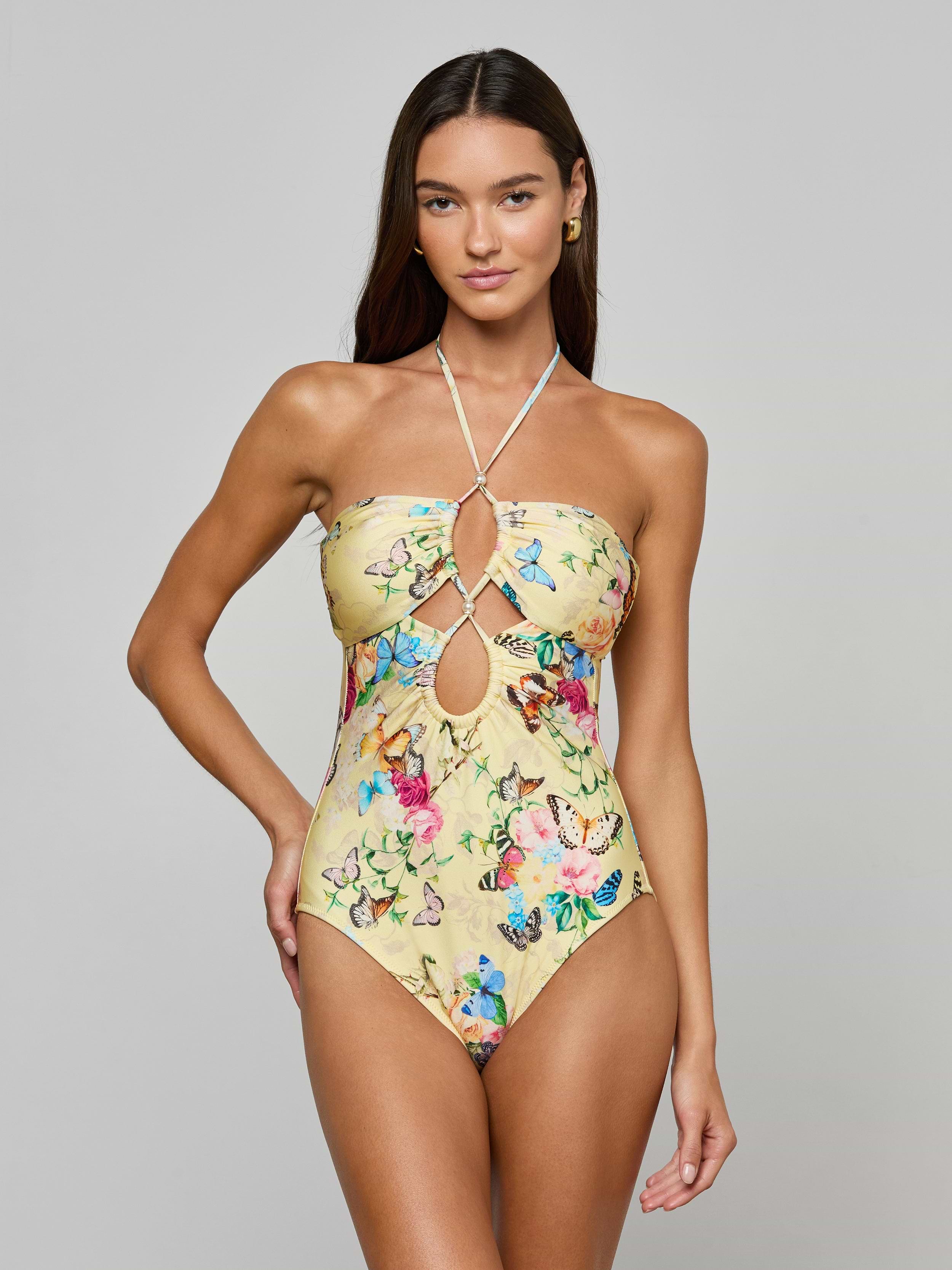 A woman models the Shiva One-Piece Swimsuit, featuring a yellow butterfly print and front keyhole cutouts, against a plain light gray background.