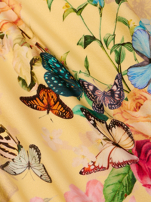 A close-up of the Shiva One-Piece Swimsuit’s yellow halter fabric, showcasing a colorful butterfly print with orange, blue, and cream butterflies amid green leaves and pastel flowers.