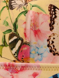 Close-up of the Lexie Bikini Top showcasing vibrant butterfly print and bright floral pattern, featuring pink, blue, and yellow flowers. The top displays visible stitching along the edge.