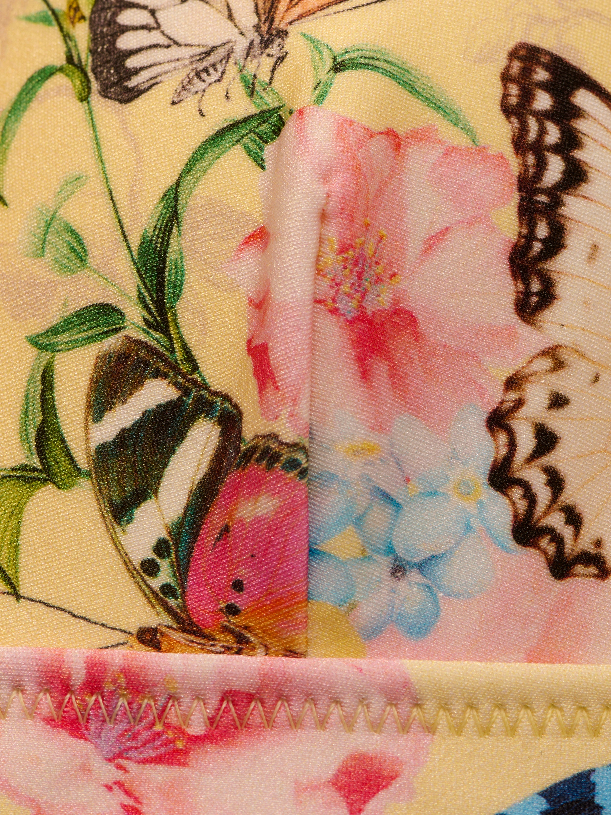 Close-up of the Lexie Bikini Top showcasing vibrant butterfly print and bright floral pattern, featuring pink, blue, and yellow flowers. The top displays visible stitching along the edge.