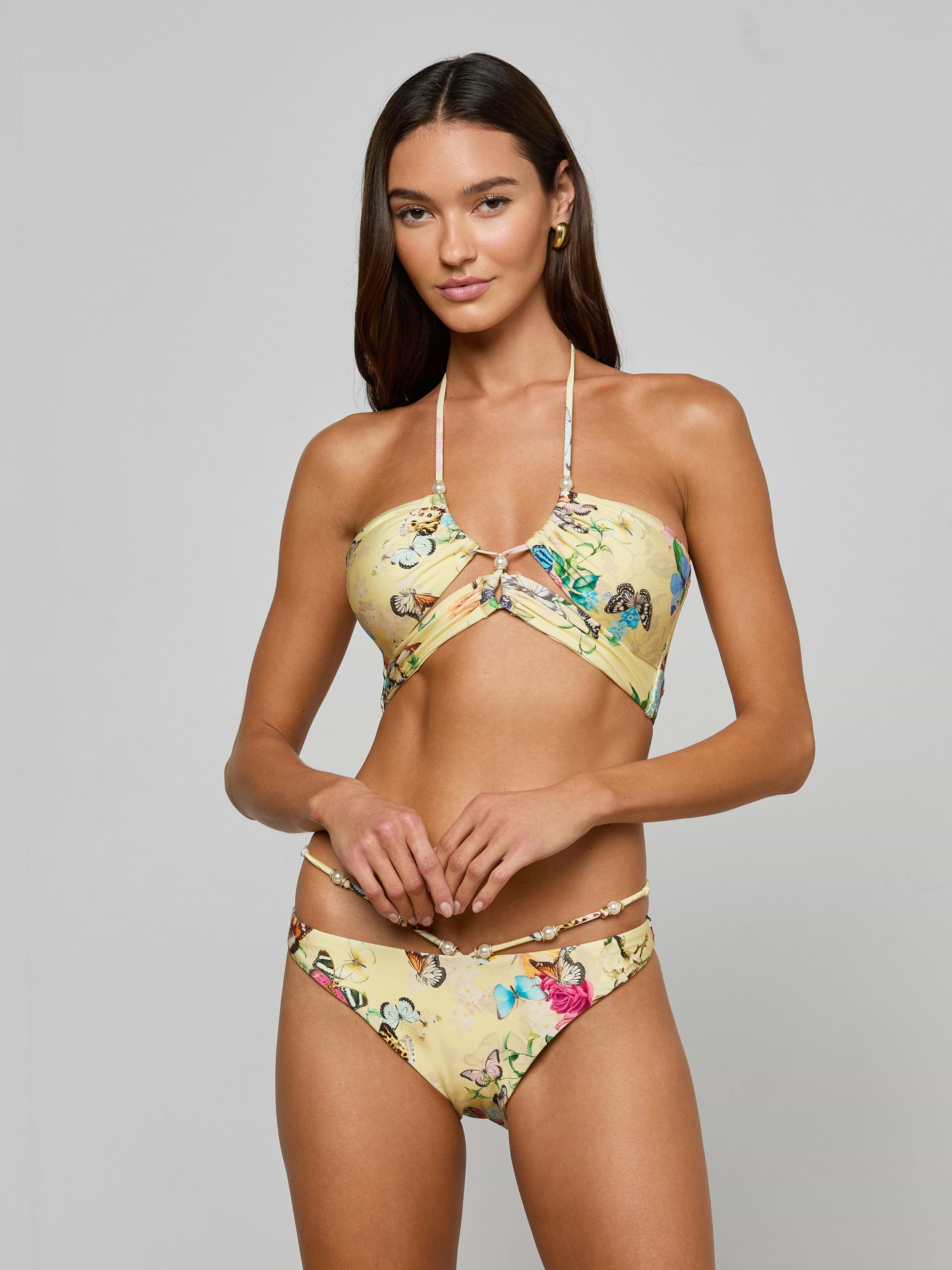 A woman with long brown hair poses against a plain background wearing the Sirena Bikini Top, a yellow butterfly print halter bikini paired with matching bottoms. She looks at the camera with a neutral expression.