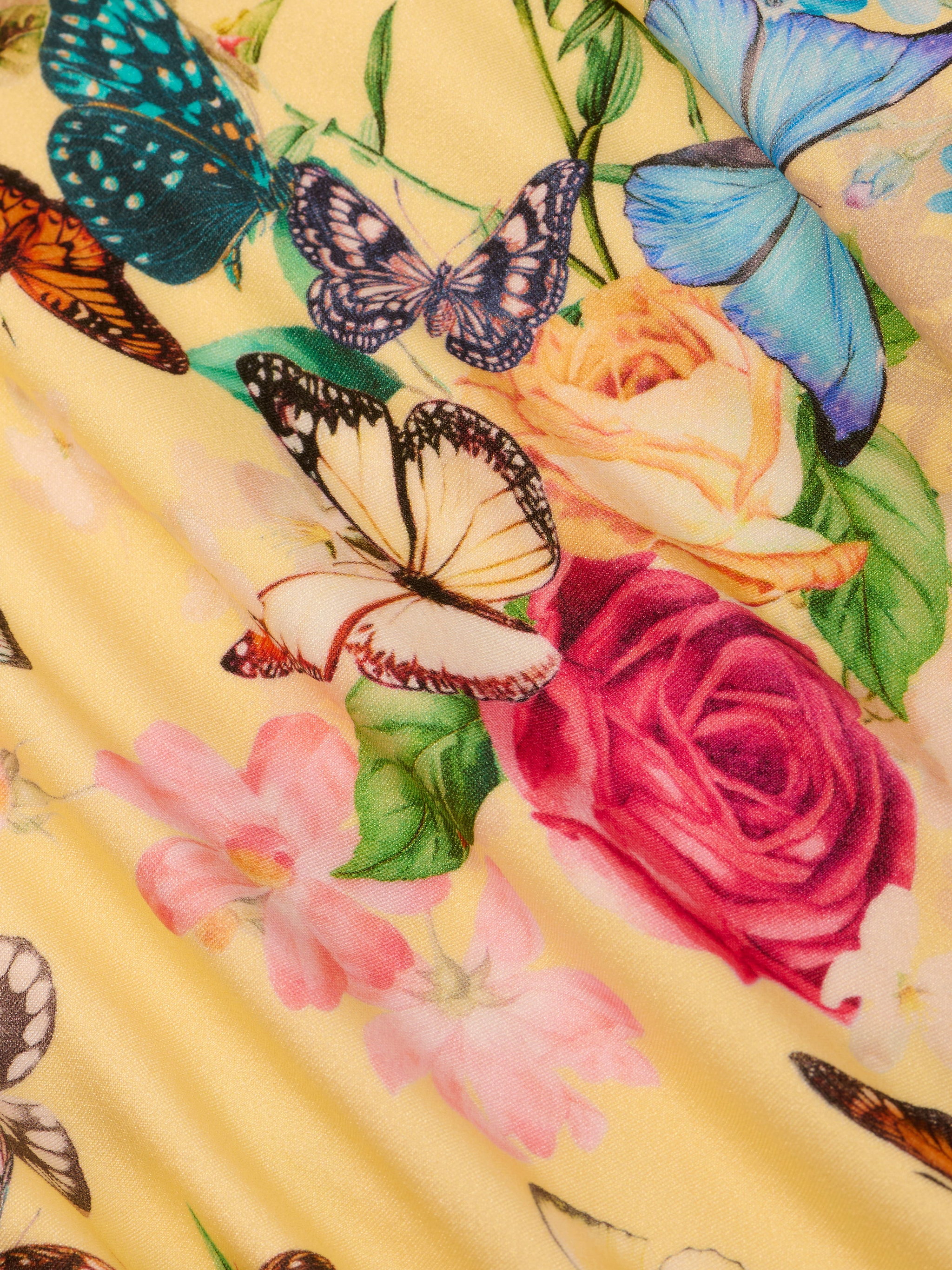 A close-up of colorful butterflies and vibrant flowers, including roses, printed on pleated yellow fabric—perfect for the Jean Bikini Bottom with a high-leg, low-rise cut.