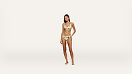 Woman standing on a plain white background, wearing a yellow bikini with a floral pattern, looking at the camera with a neutral expression and one hand resting on her hip.