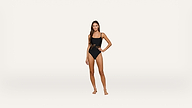 A woman stands barefoot in a black one-piece swimsuit with lace-up detailing on the side, posing against a plain white background.