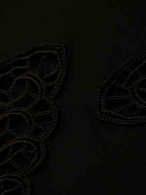 Close-up of the Remi One-Piece Swimsuit in black, showcasing intricate embroidery and subtle crochet appliqué with geometric and scalloped patterns, all stitched with black thread on a smooth, dark fabric.