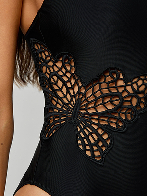 A close-up of the Remi One-Piece Swimsuit in black, showcasing an intricate sheer butterfly cutout on the side that reveals skin beneath the pattern, plus removable cups for customizable support.
