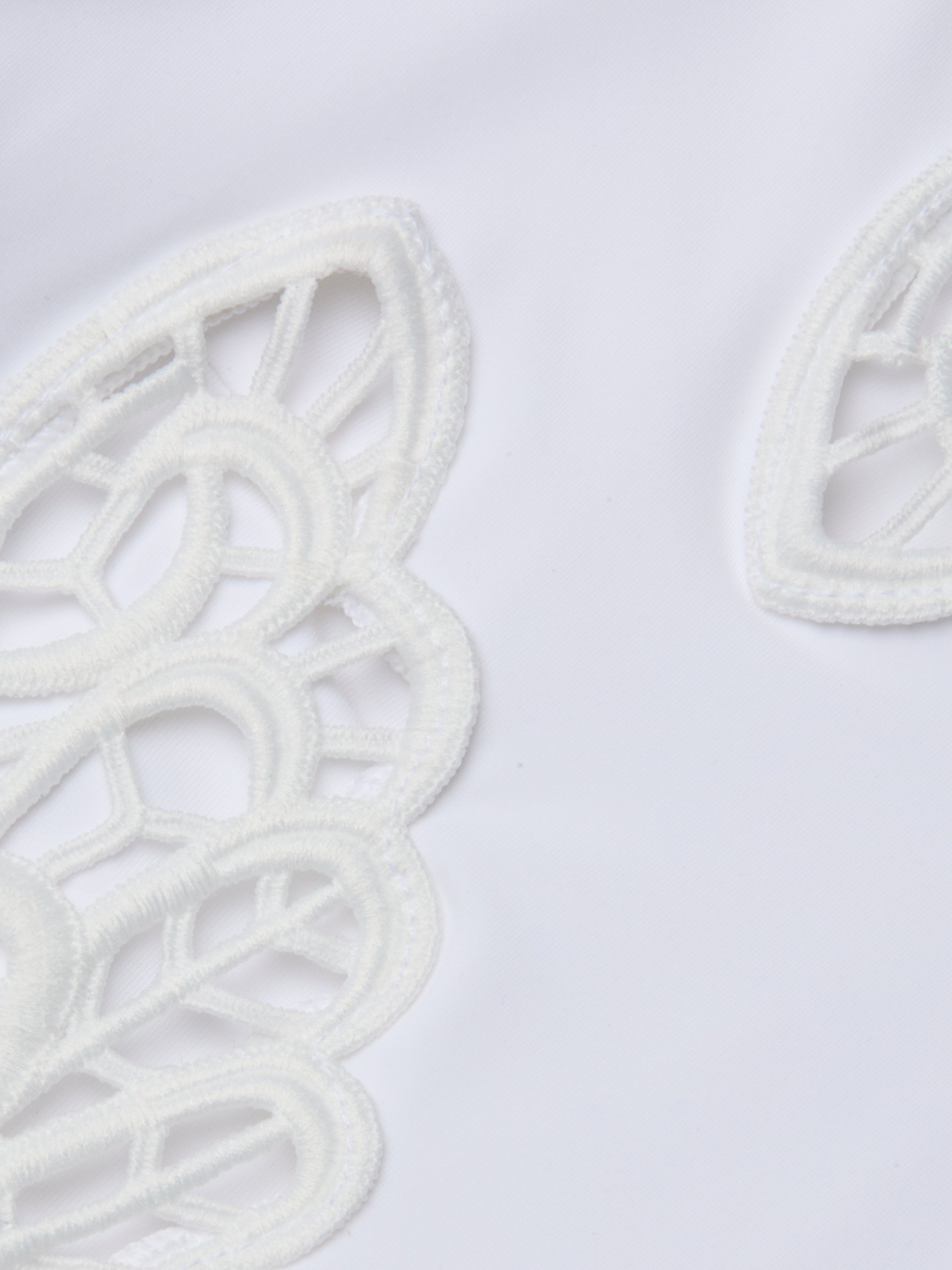 Gros plan sur le tissu blanc du maillot de bain une pièce Remi, qui présente des découpes brodées décoratives aux formes incurvées semblables à des pétales et des applications de papillons pour un look délicat inspiré de la dentelle.