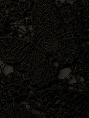 Close-up of intricate black lace fabric on the Geraldine Cover-Up Pant, featuring a detailed butterfly motif and woven textures that create a delicate, elegant look against a dark background.