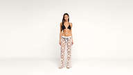 A woman stands against a plain white background, wearing a black bikini top and sheer white lace pants with a floral pattern and black waistband.