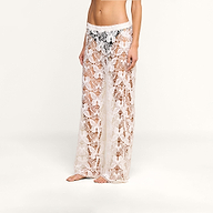 A person wearing the Geraldine Cover-Up Pant, featuring a sheer white bohemian crochet lace design with a floral pattern, stands barefoot against a plain white background.