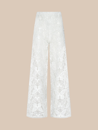 The Geraldine Cover-Up Pant showcases effortless resort wear elegance with its white lace wide-leg silhouette, high waist, and delicate floral pattern set on sheer fabric against a plain beige background. These bohemian pants exude relaxed sophistication, making them perfect for sun-soaked escapes.