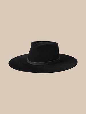 Il cappello Fedora con fascia in pelle Reyes presenta unampia tesa in feltro nero, una calotta piatta e unelegante fascia in pelle nera, il tutto su uno sfondo beige a tinta unita.