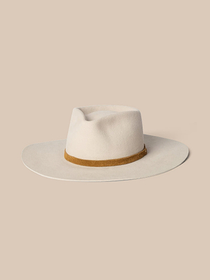 The Reyes Leather Band Fedora by Gladys Tamez Millinery features a cream felt wide brim and a light brown leather band, showcased against a beige background.