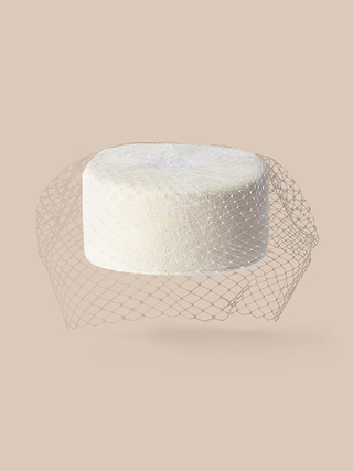 Il cappello Pillbox di Anstine, un cappello rotondo bianco parzialmente ricoperto da una rete ampia in stile birdcage, è esposto su uno sfondo beige a tinta unita, evocando uneleganza vintage.