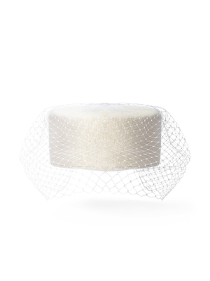 The Anstine Pillbox Hat, shown against a plain white background, features a round white form covered with a fine mesh net reminiscent of a birdcage veil.