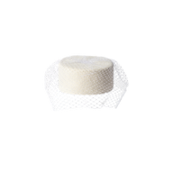 The Anstine Pillbox Hat, a round white accessory with a delicate mesh net partially draped over it—evoking the refined textures characteristic of millinery and classic pillbox hats—is displayed against a plain white background.