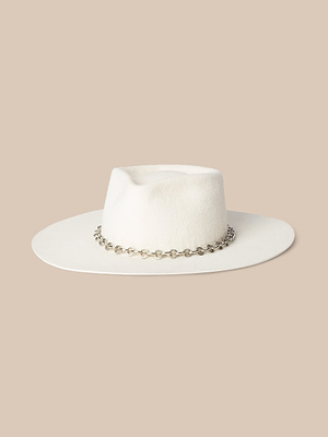 The Umbra Hat, handcrafted in LA from white felt velour, features a wide brim, a teardrop crown, and a silver chain at the base, shown against a beige background.