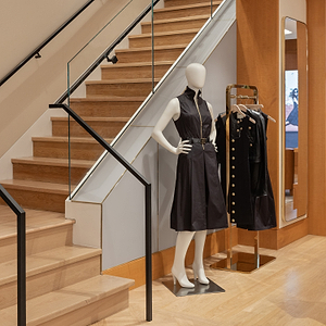 Mannequin wearing a black dress in a store setting with wooden stairs and clothing rack.