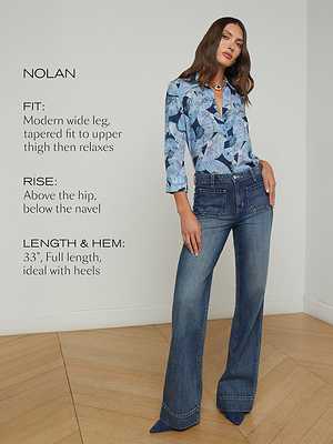 A woman wearing a blue patterned blouse and wide-leg jeans stands in a bright room. Text beside her describes the Nolan jeans: modern wide leg, tapered fit, rise above the hip, and 33 full-length ideal for heels.