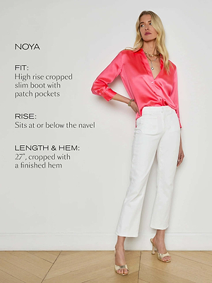A woman stands against a white wall wearing a bright pink satin blouse, beige heeled sandals, and Noya Cropped Slim Flare Jeans. Text beside her highlights the jeans’ slim flare fit, high rise, cropped length, and finished hem.