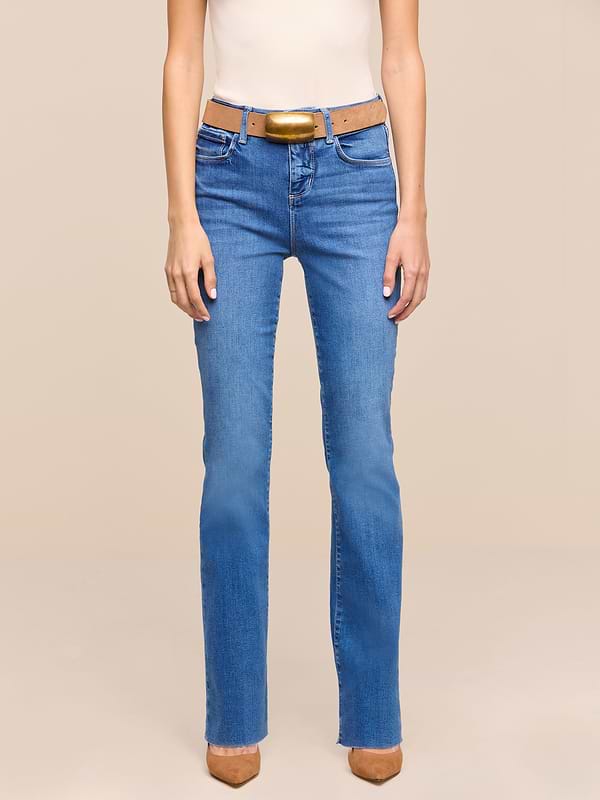A person is shown from the shoulders down, wearing a sleeveless beige top, a brown belt, brown pointed-toe shoes, and heritage indigo wash Petite Ruth Straight-Leg Jean, standing against a plain white background.