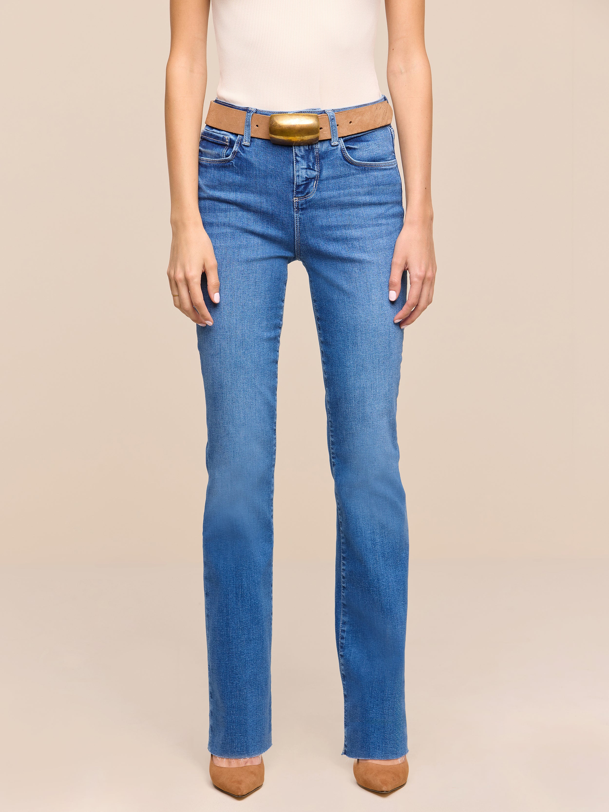 A person is shown from the shoulders down, wearing a sleeveless beige top, a brown belt, brown pointed-toe shoes, and heritage indigo wash Petite Ruth Straight-Leg Jean, standing against a plain white background.