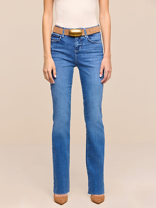 A person wearing the Petite Ruth Straight-Leg Jean in a heritage indigo wash, paired with a light brown belt, a white sleeveless top, and tan heeled shoes, standing against a plain beige background.