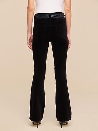 A person wearing the Petite Stevie Velvet Jean in black and a white sleeveless top is standing with their back to the camera against a plain beige background, highlighting the jean’s high-rise, slim straight-leg silhouette.