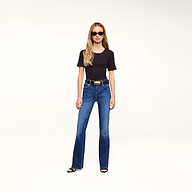 A woman in sunglasses, a black t-shirt, and black heels stands against a plain white background, wearing the Petite Selma Bootcut Jean.