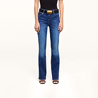 A person wearing a black sleeveless top, the Petite Selma Bootcut Jean in blue super stretch denim, a black belt with a gold buckle, and black heeled sandals stands against a plain white background.