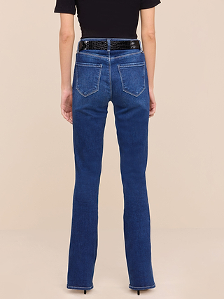 A person shown from the back against a plain beige background wears the Petite Selma Bootcut Jean from the Les Petites Collection in high-waisted, dark blue super stretch denim, styled with a black belt and black top.