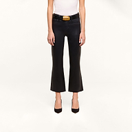 Person wearing a white sleeveless top and the Petite Kendra Coated Jean—black high-rise flared pants styled with a wide black belt featuring a gold buckle—and black pointed-toe heels, standing against a plain white background.