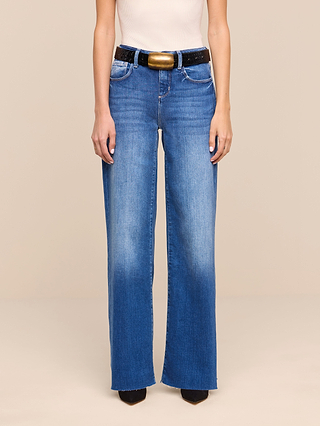 A person wearing the Petite Scottie Wide-Leg Jean in an indigo wash from the Les Petites Collection, styled with a dark belt, cream sleeveless top, and black pointed shoes, standing against a plain beige background.