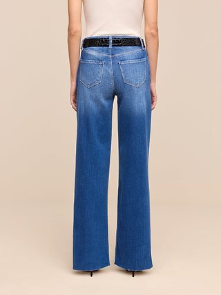 A person wearing the Petite Scottie Wide-Leg Jean from the Les Petites Collection in a high-waisted indigo wash, styled with a black textured belt and sleeveless white top, shown from the back against a plain beige background.