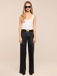 A woman with long blonde hair wears black sunglasses, a white tank top, and the Petite Scottie Coated Jean with a belt and black shoes, standing against a plain white background.
