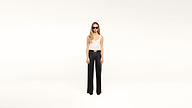 A woman wearing sunglasses, a white tank top, and black wide-leg pants paired with a stylish black belt stands confidently against a plain white background.