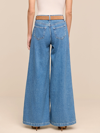 From the Les Petites Collection, a person seen from behind stands against a beige background, wearing the Petite Quincy Wide-Leg Jean in denim blue with an exposed waistband and back pockets.