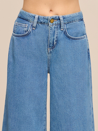 A person is wearing the Petite Quincy Wide-Leg Jean from the Les Petites Collection—a high-waisted, wide-leg blue jean made from featherweight denim, designed with front pockets and a button closure. Only the jeans and lower torso are visible against a neutral background.