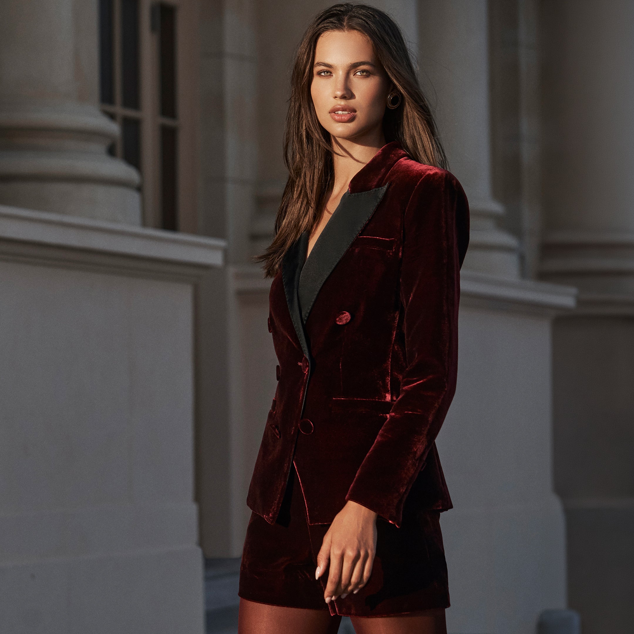 A person wearing a burgundy velvet Kyomi Velvet Blazer with black lapels and matching tailored shorts.