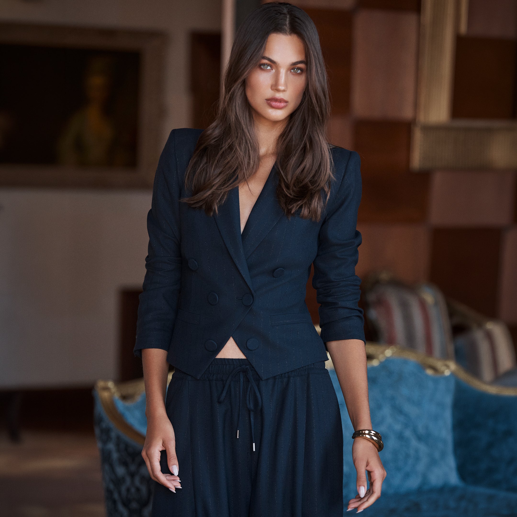 A woman wearing a dark blue, double-breasted Risa Double-Breasted Blazer with three-quarter sleeves and matching tailored trousers with a drawstring waist.